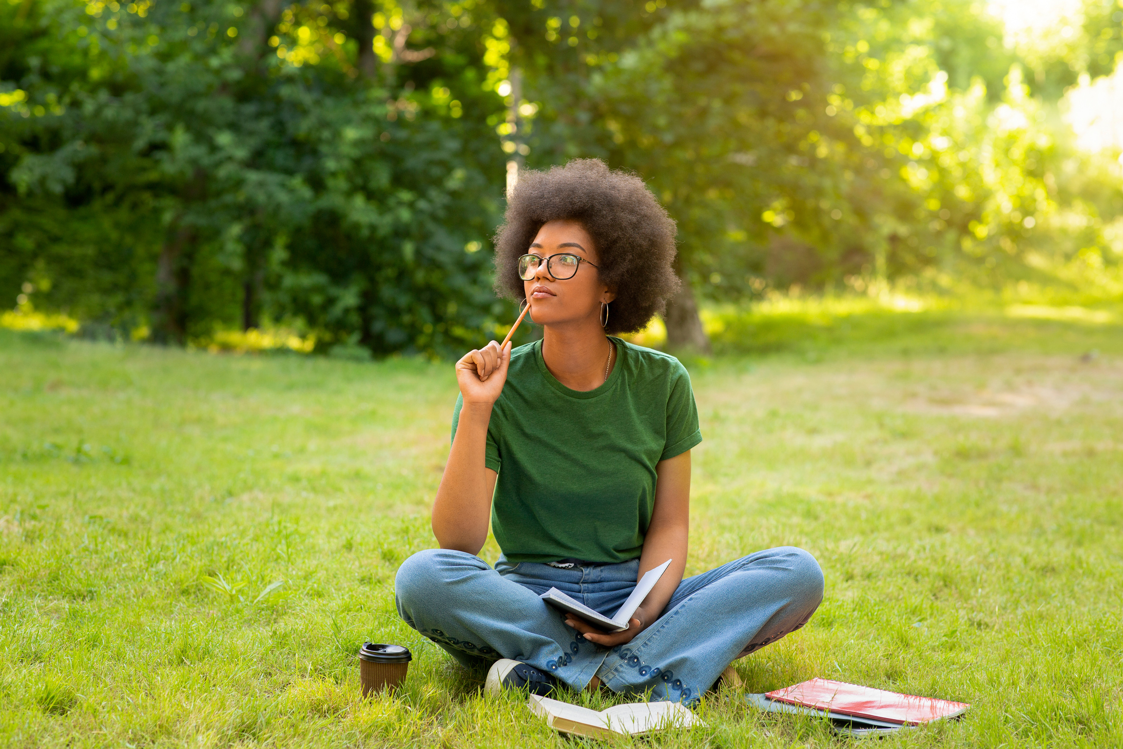 Thoughtful black student girl sitting outdoors, writing essay for college classes